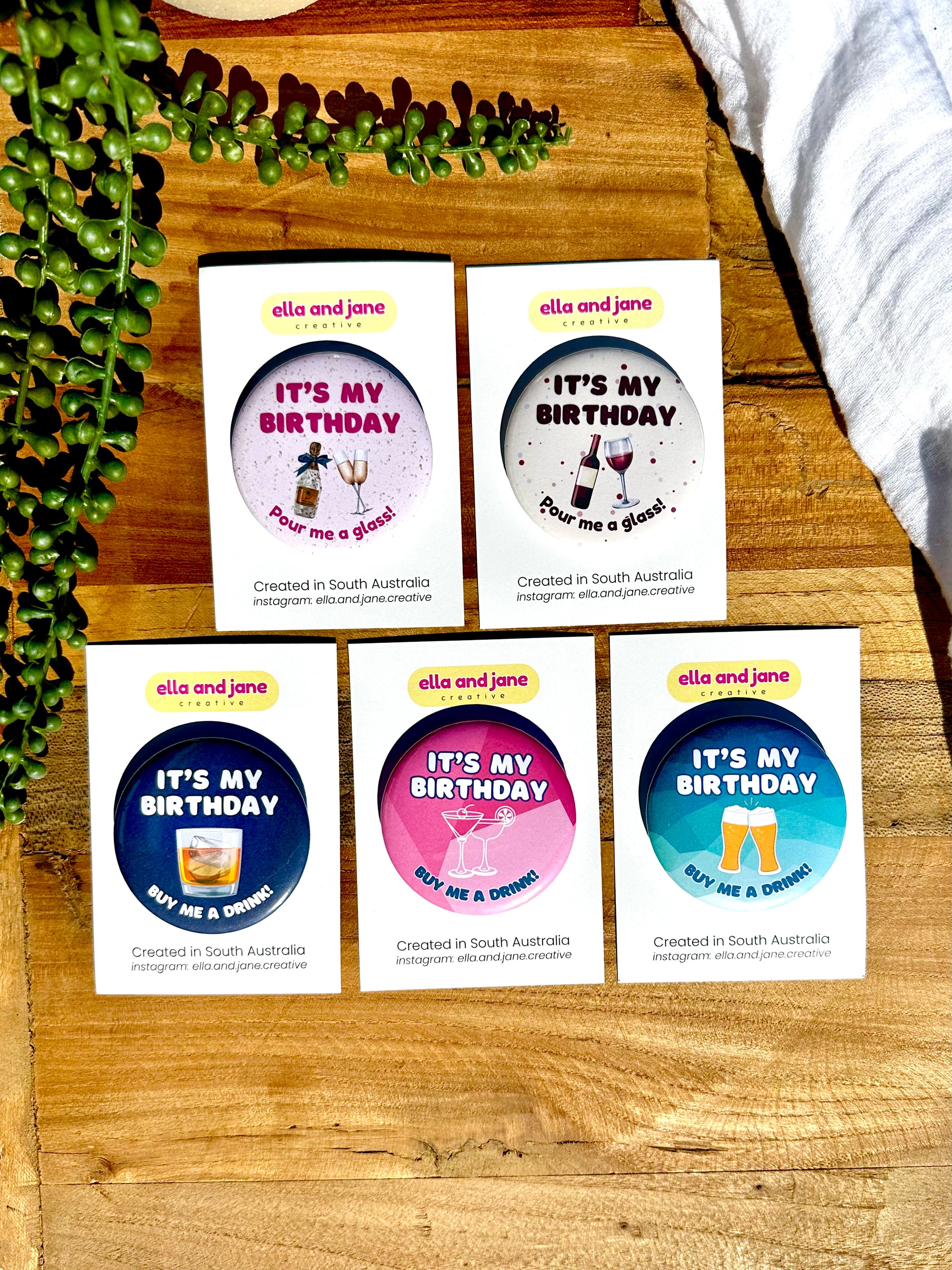 5 birthday badges - Pink badge with It's My Birthday Pour me a glass with a picture of champagne glasses and wine bottle. Cream birthday badge with It's My Birthday Pour me a glass! with a bottle of red wine and wine glasses. Three other birthday badges all with It's My Birthday Buy Me A Drink! as text. One is a navy blue background with a picture of a scotch glass. The other is a pink background with picture of two cocktails glasses. The third is a medium blue background with two beer glasses.