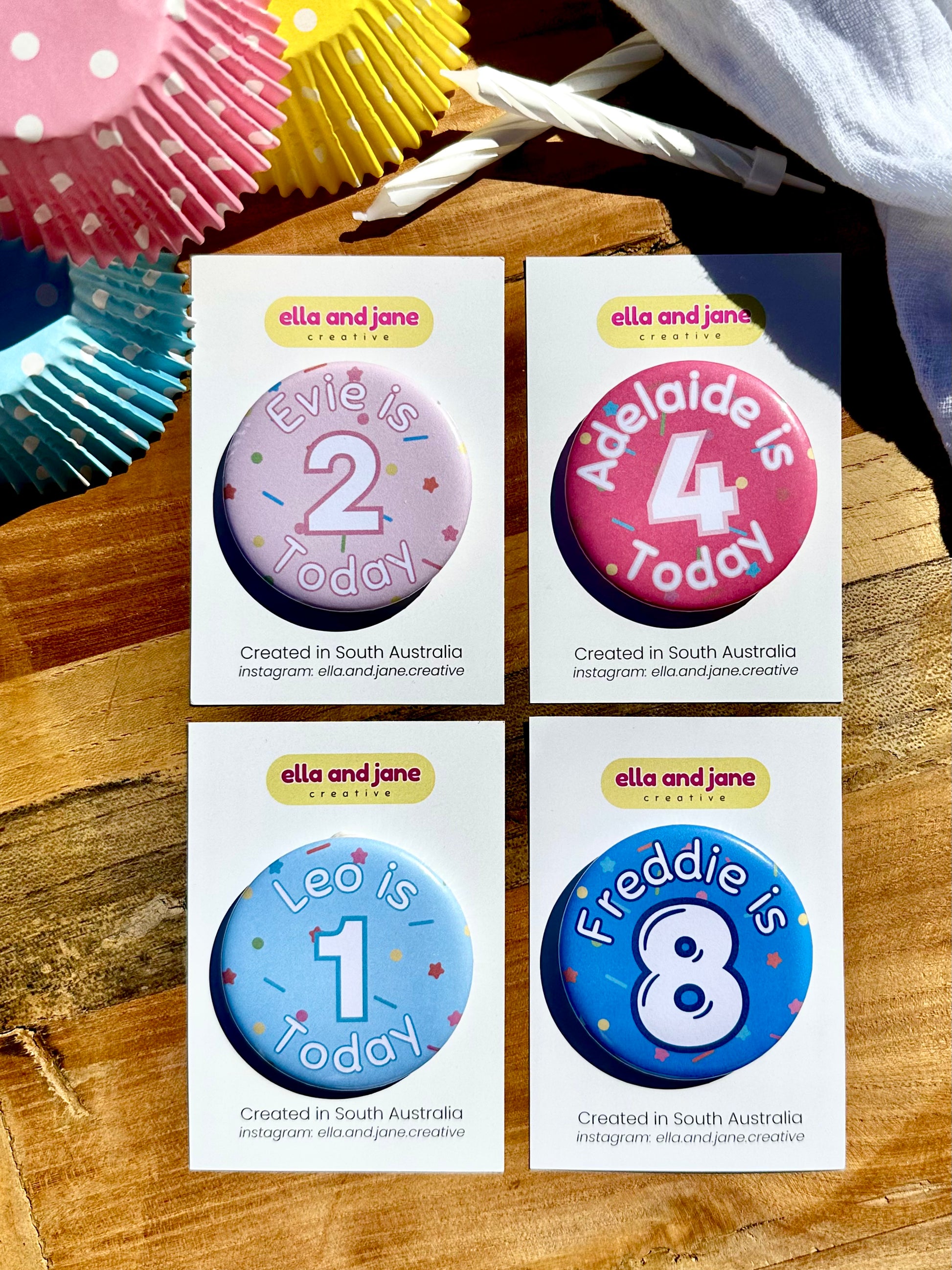 Four birthday party badges. A light pink badge with sprinkles as the background. The Text is in white and pink 'Evie is 2 Today'. A medium pink badge with sprinkles as the background. The text is in white and pink 'Adelaide is 4 Today'. A light blue birthday badge with sprinkles as the background. Text in white and blue 'Leo is 1 Today' and a medium blue birthday badge with sprinkles in the background. The text is 'Freddie is 8' in white and dark blue.