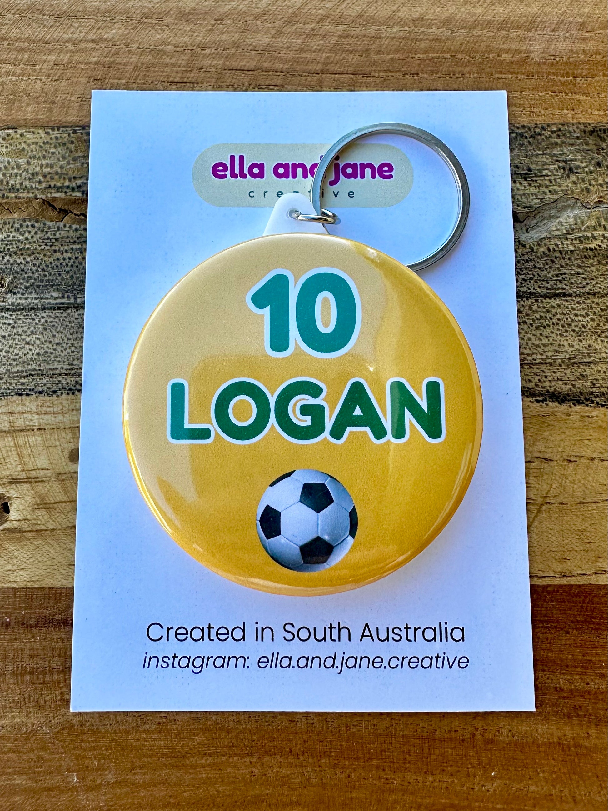 A bright yellow, round keyring with the number '10' in green and the name 'logan' also in green. There is an image of a soccer ball.