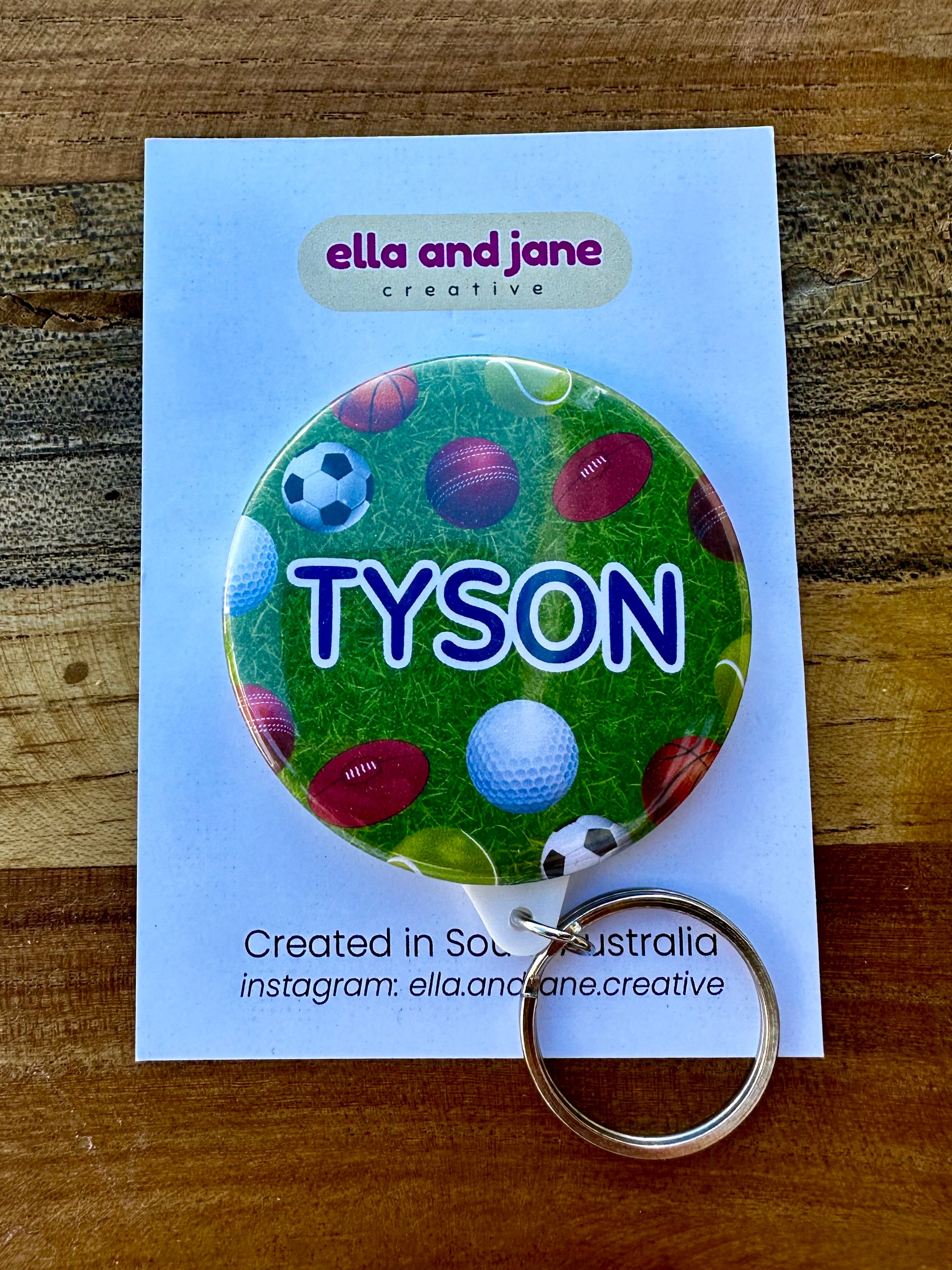 A round keyring with the name 'Tyson' and a green grass background. There are various sporting balls inlcuding soccer, football, gold, tennis, basketball and cricket.